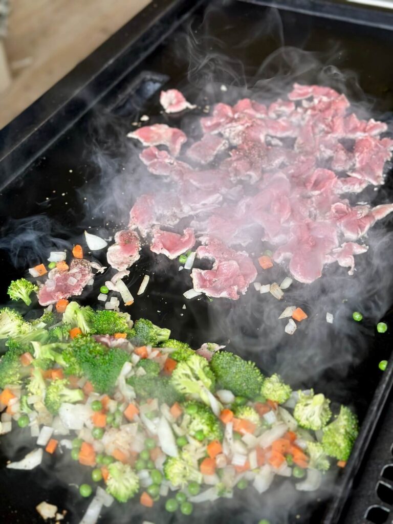 cooking slices of pork and vegetables on a griddle