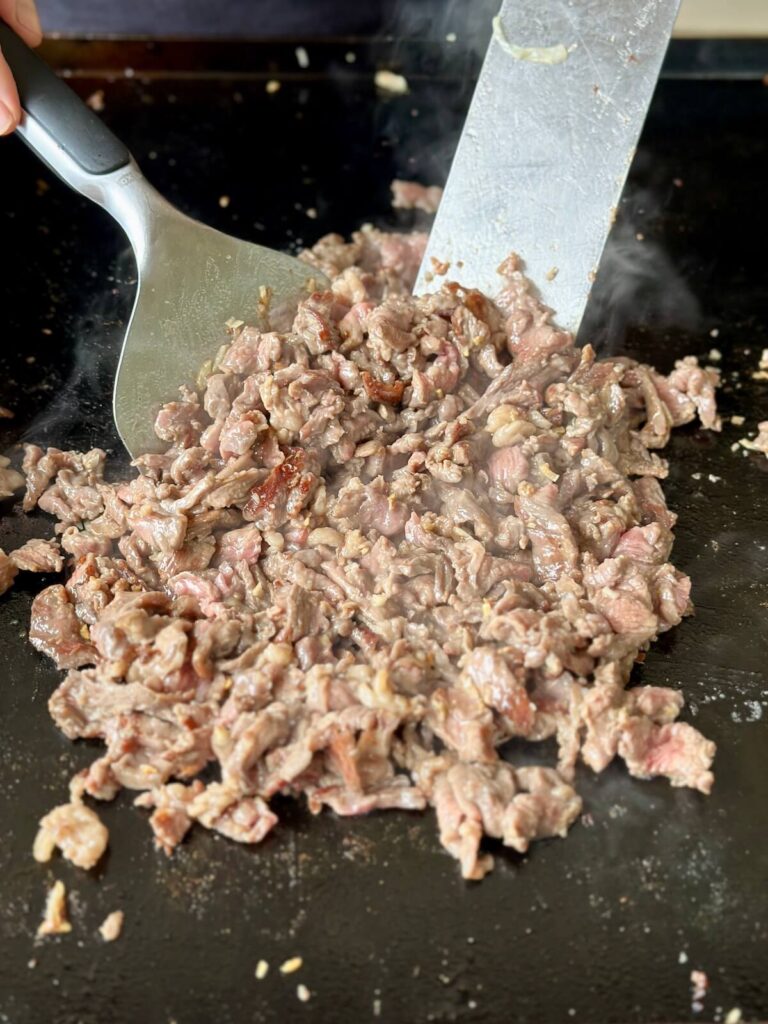 using a bent handle scraper for the griddle to cook taco meat