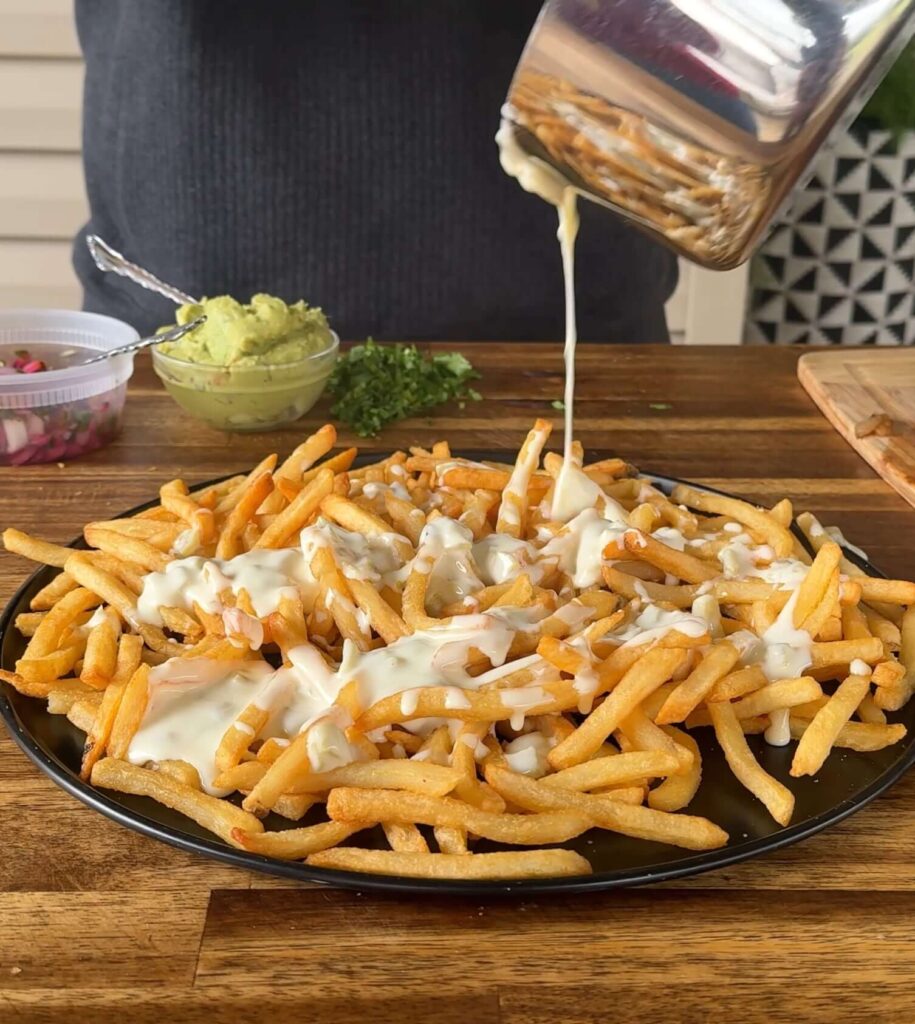 pouring homemade white cheese dip on french fries