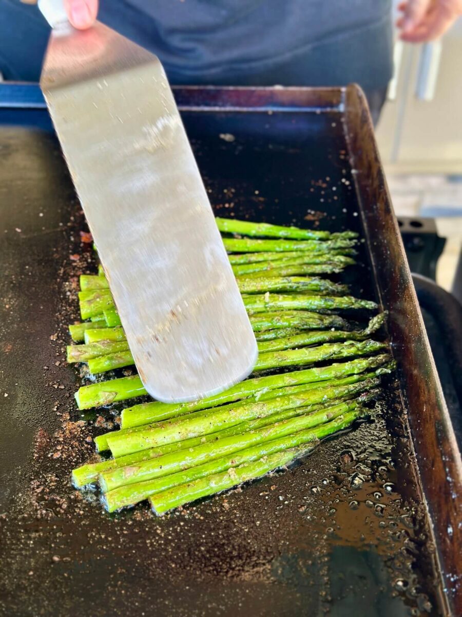 using a spatula to roll asparagus on Blackstone griddle