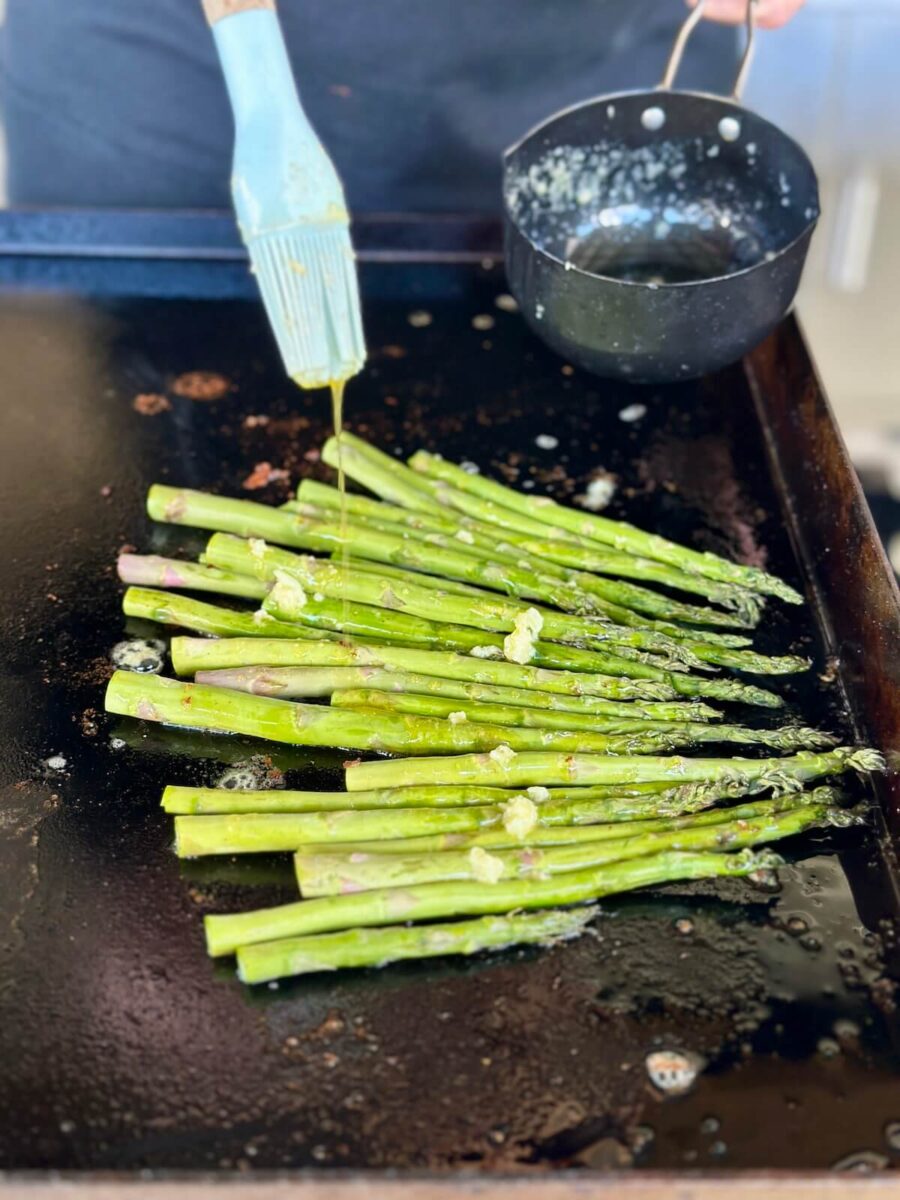 adding garlic butter to asparagus on a griddle
