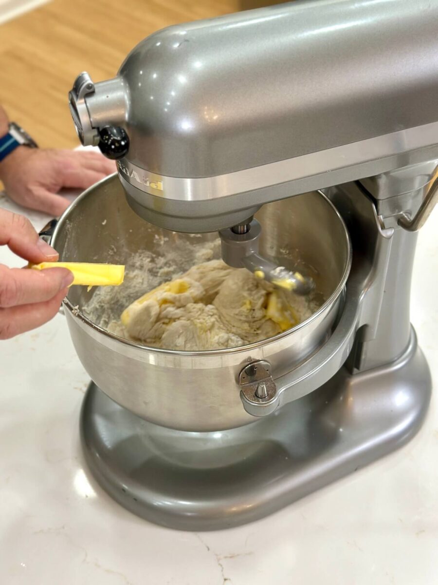 adding butter to a mixing bowl with hoagie roll dough