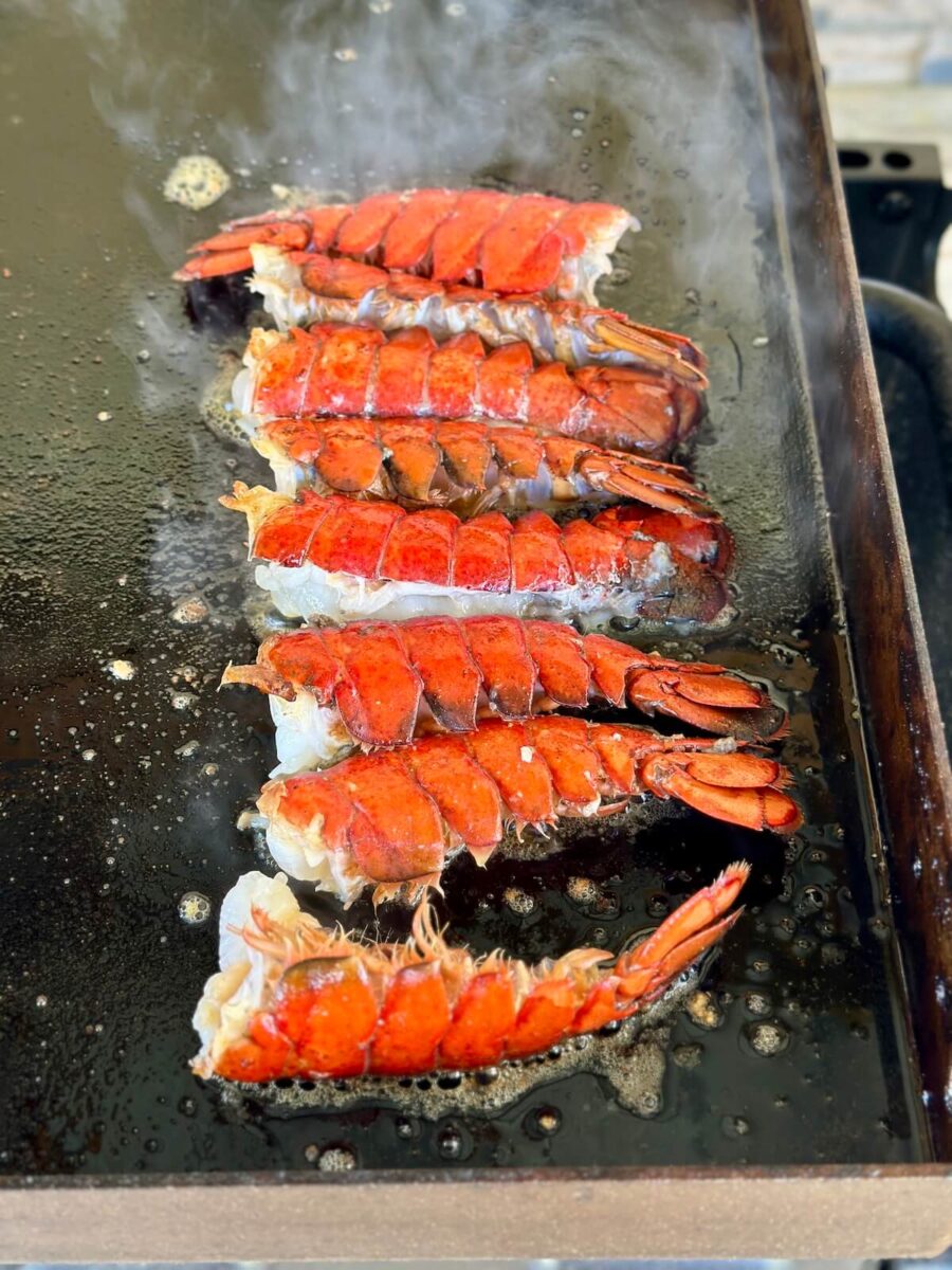 lobster tails cooking meat side down on a griddle