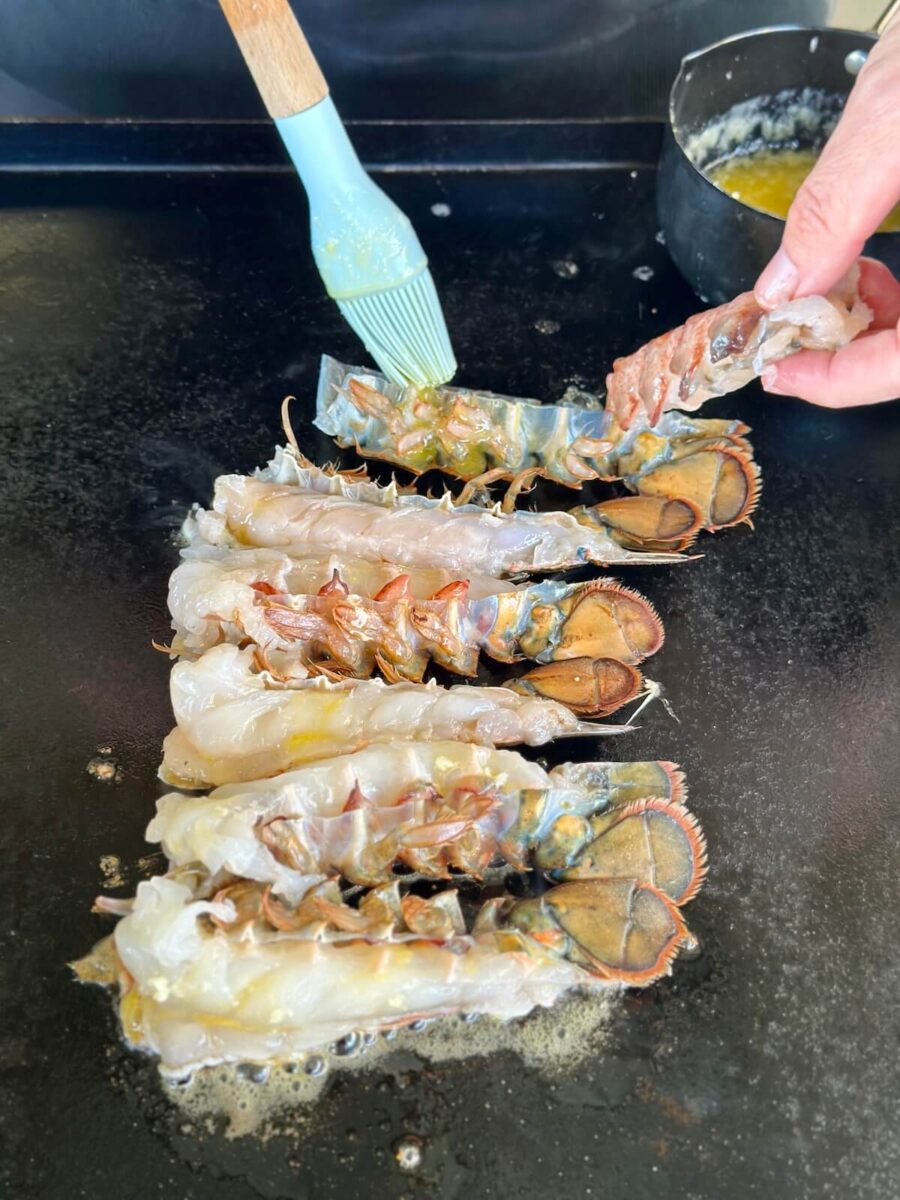 adding melted butter to the shell of a split lobster tail on the griddle