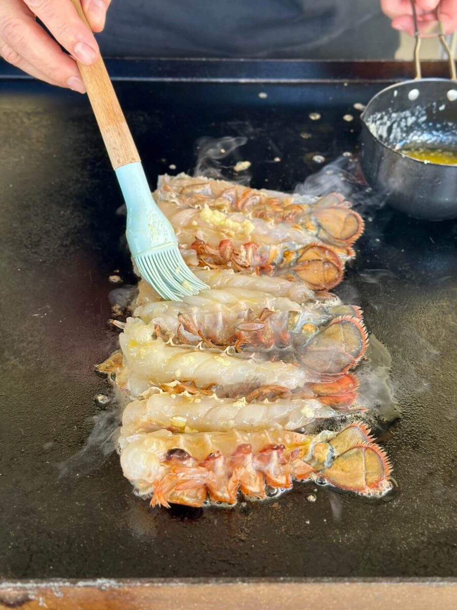 brushing garlic butter over lobster tails on the Blackstone griddle