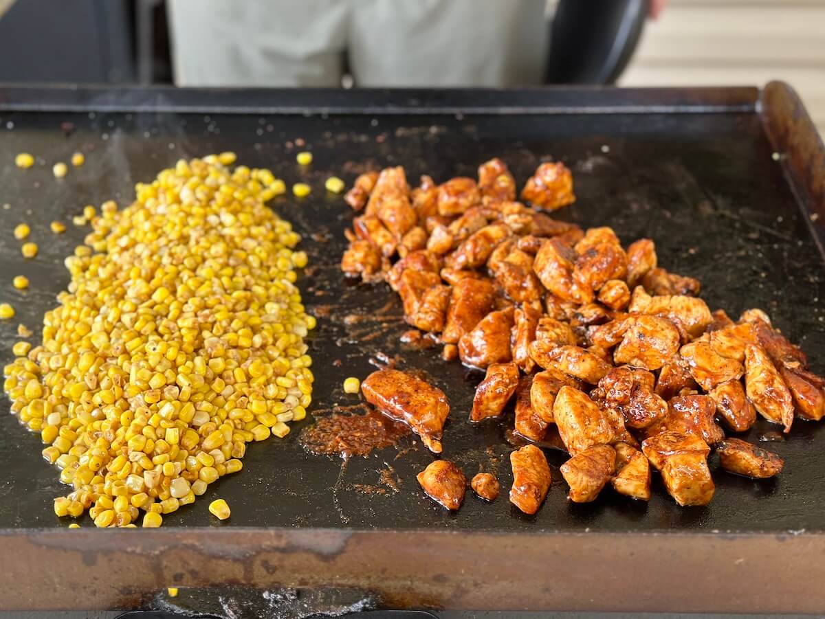 BBQ chicken bites and buttered corn cooking on a griddle