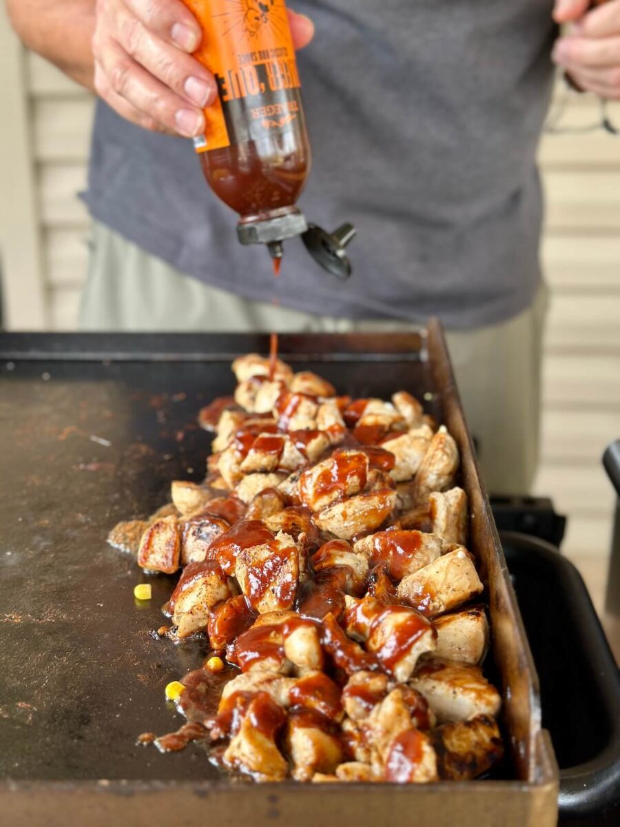 adding BBQ sauce to chicken bites on a griddle