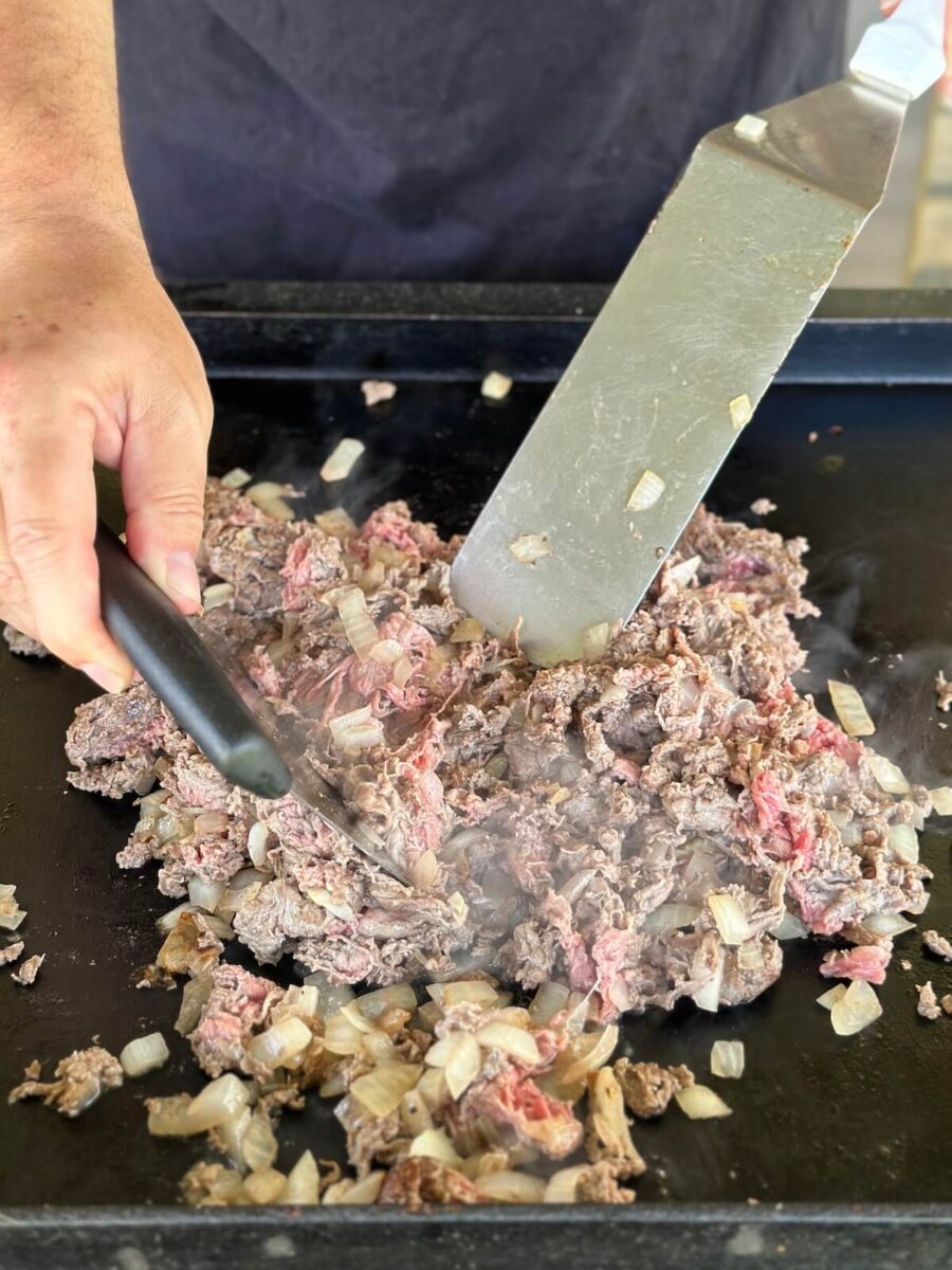 mixing diced sauteed onions with thinly sliced ribeye steak