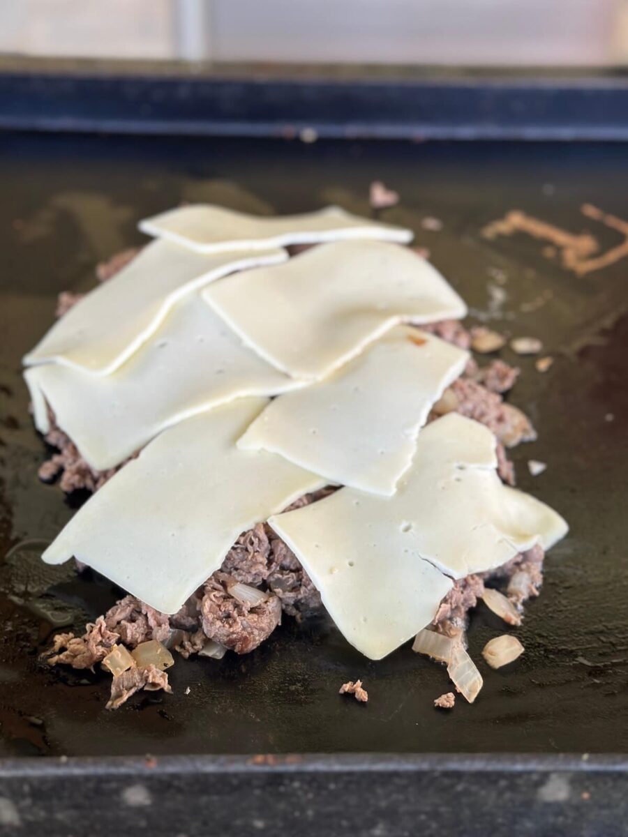 sliced white American cheese melting on top of a pile of sliced ribeye steak