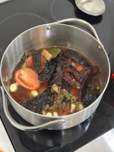 stewing chile peppers, roma tomatoes, garlic, onion, and spices in a pot on the stove