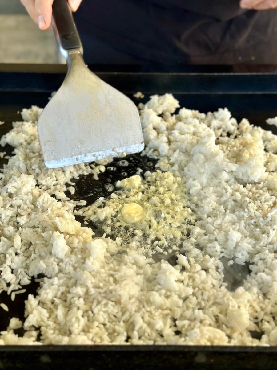 heating butter and minced garlic in the middle of a pile of white rice on a griddle