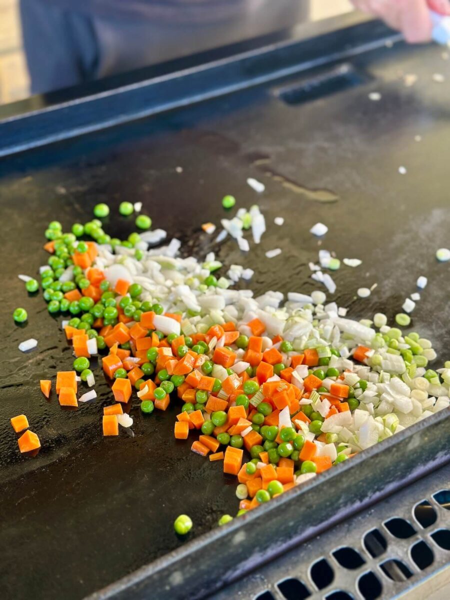 sautéing peas, carrots, and diced onions on a griddle