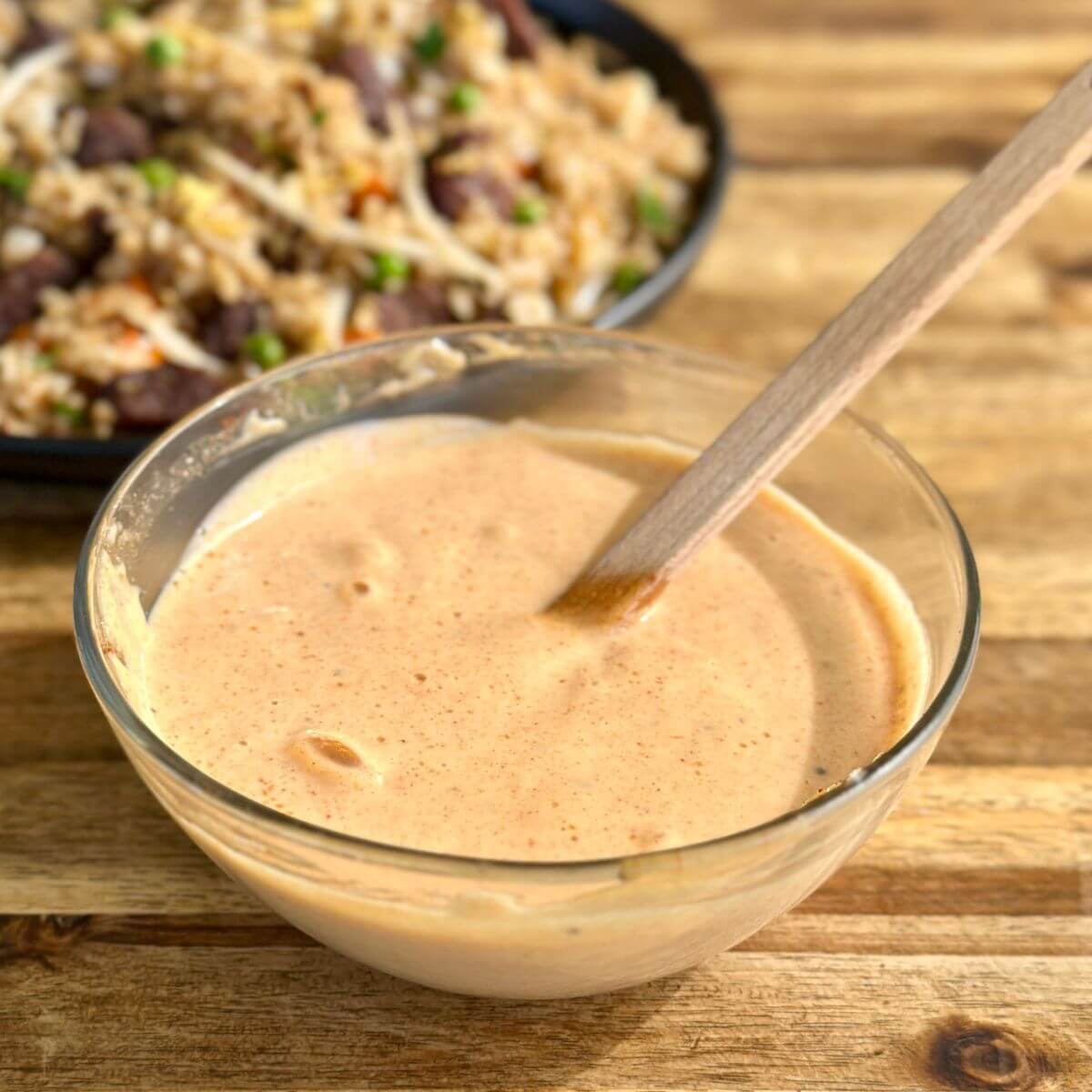 yum yum sauce in a bowl with a plate of fried rice in the background