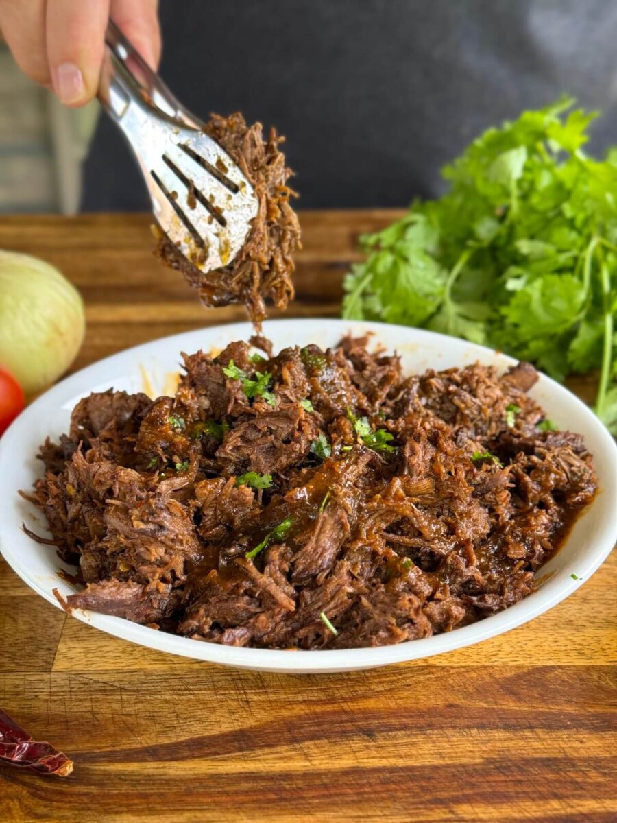man using tongs to serve beef birria meat