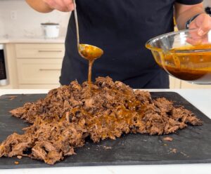 ladling birria sauce over shredded beef
