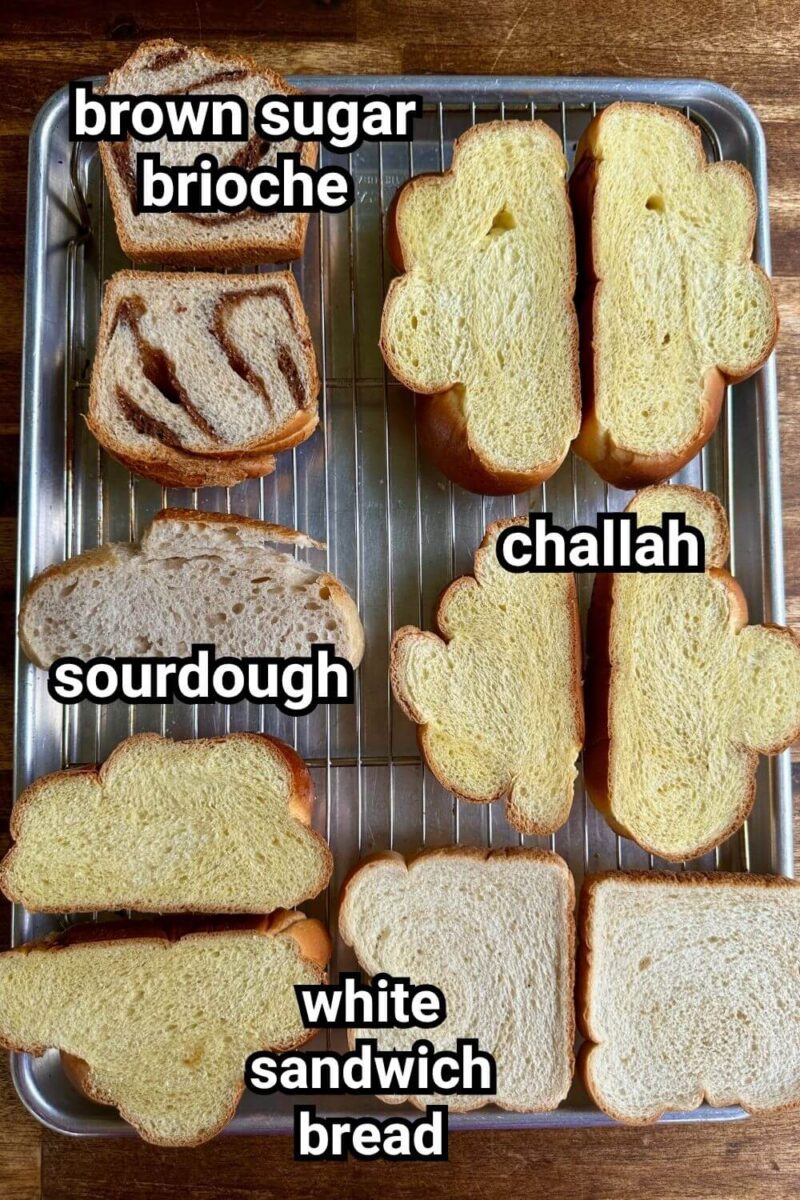 4 different types of bread drying on a wire cooling rack including challah, sourdough, brioche, and white bread
