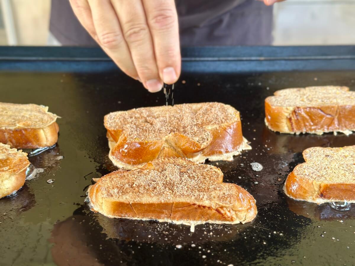 sprinkling cinnamon sugar mix on top of french toast on the Blackstone griddle