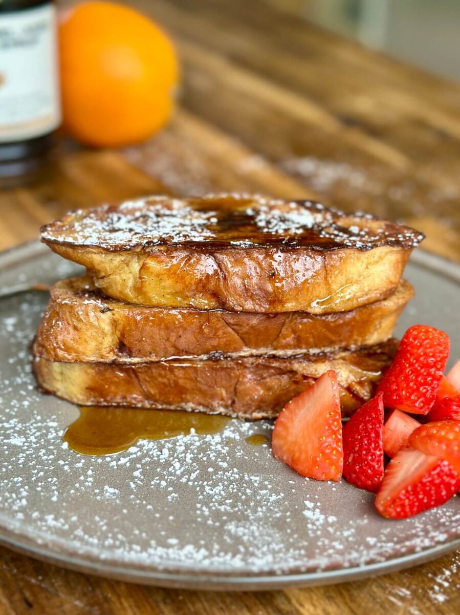 French toast stacked up on a plate with powdered sugar and syrup on top