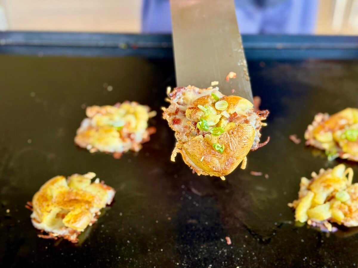 using a griddle spatula to remove a smashed potato from a Blackstone griddle