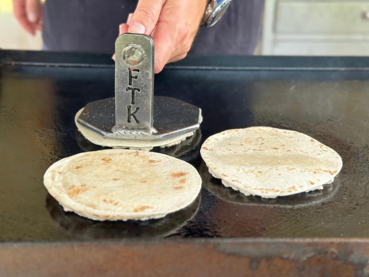 smashing ground chicken and tortillas on a griddle