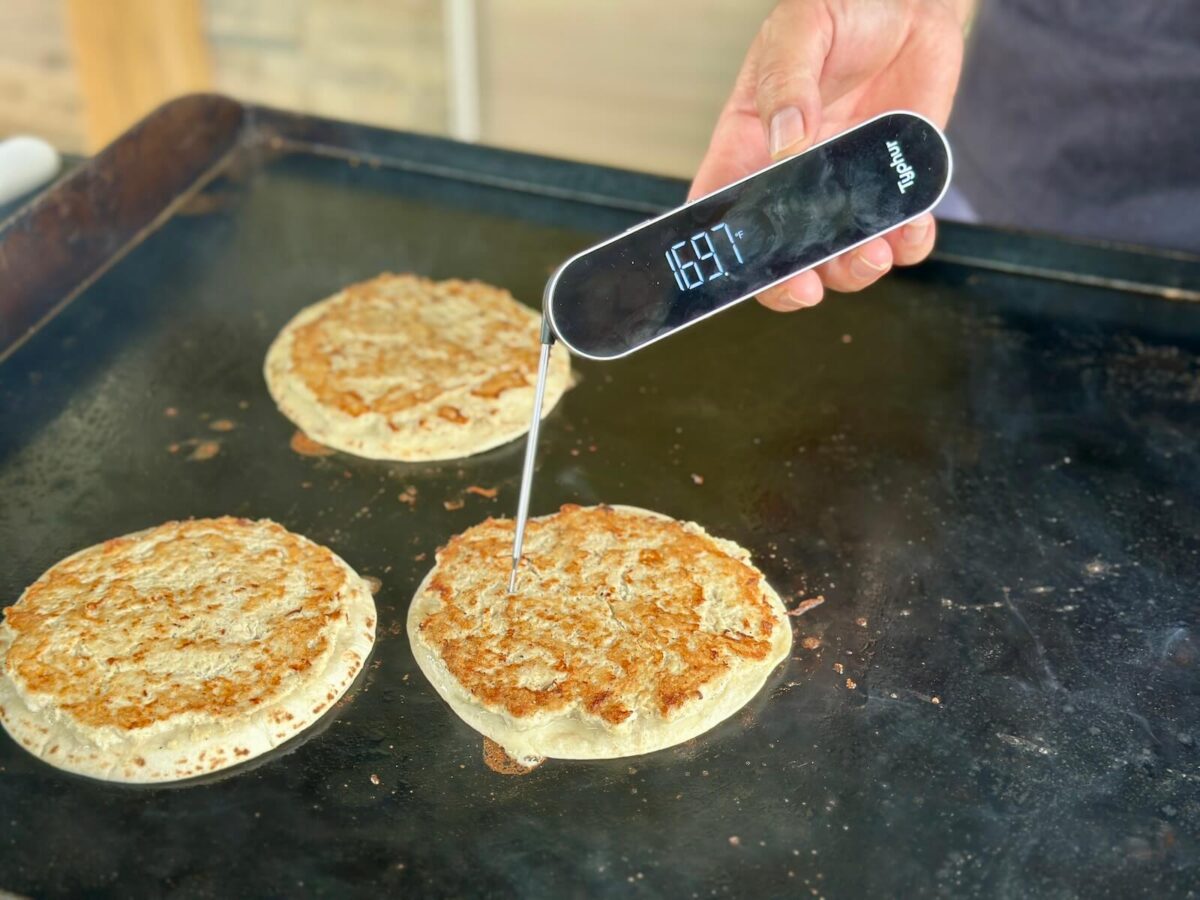 using an instant read thermometer to check the temperature of chicken smash tacos on a Blackstone