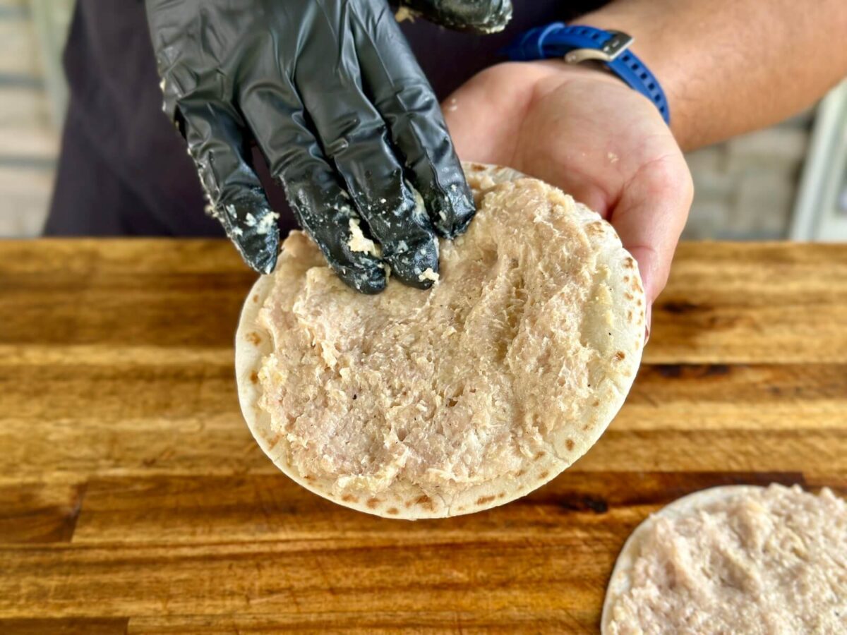 spreading a ground chicken mixture on a flour tortilla