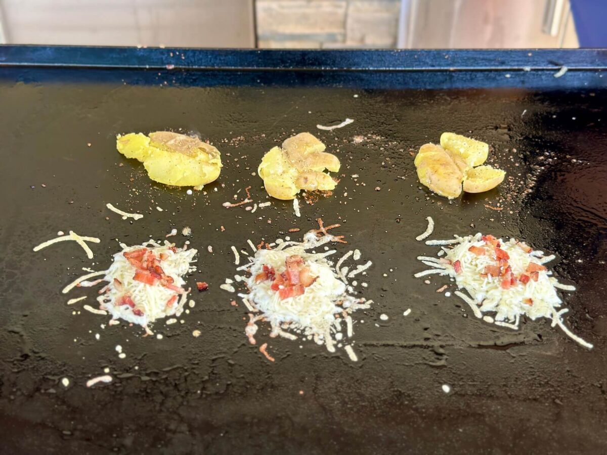 smashed potatoes and piles of parmesan cheese cooking on a Blackstone griddle