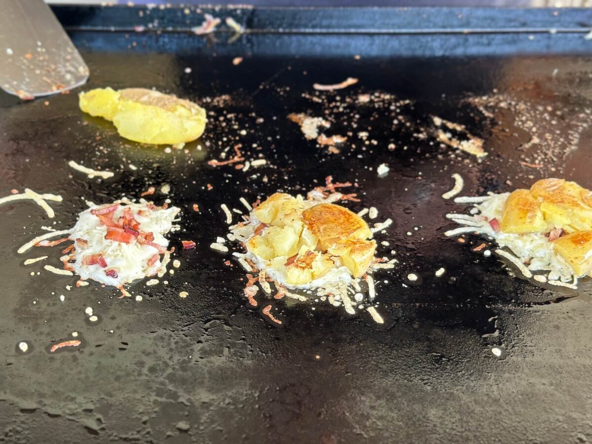 smashed potatoes on top of small piles of parmesan cheese on a griddle