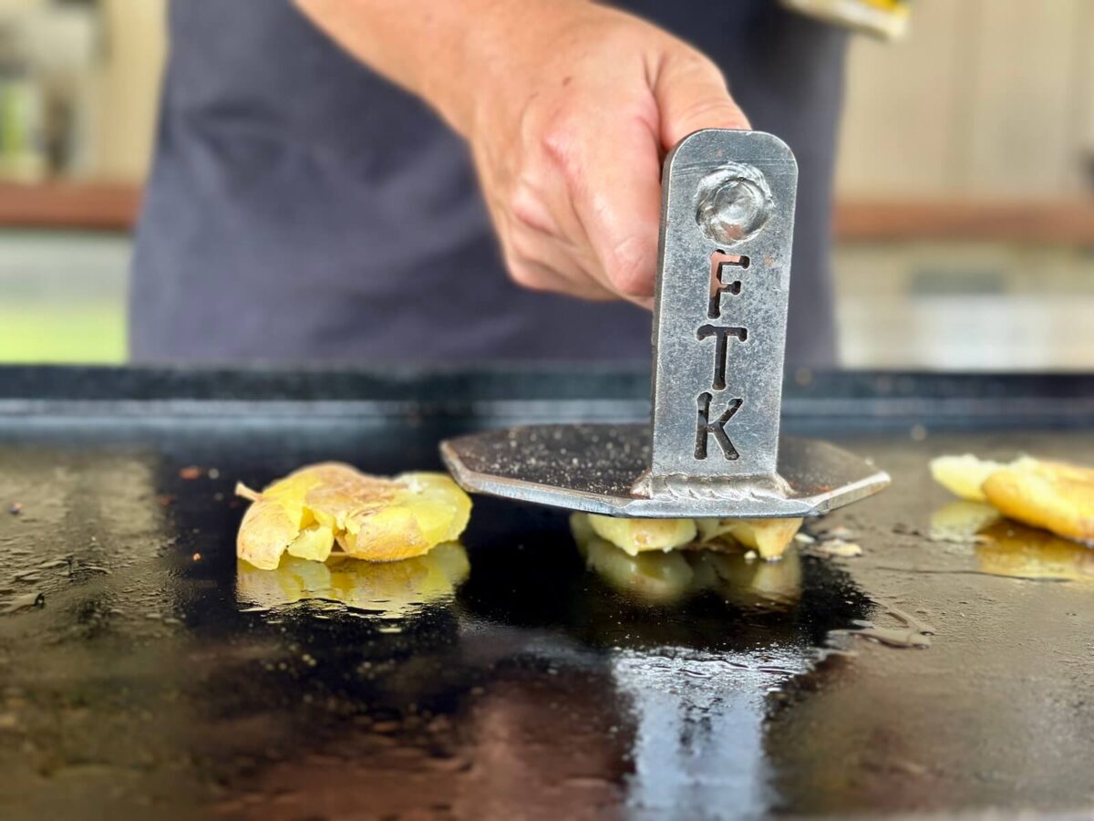 using a burger press to smash potatoes on a Blackstone griddle