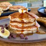banana chocolate chip pancakes with syrup and butter on a plate