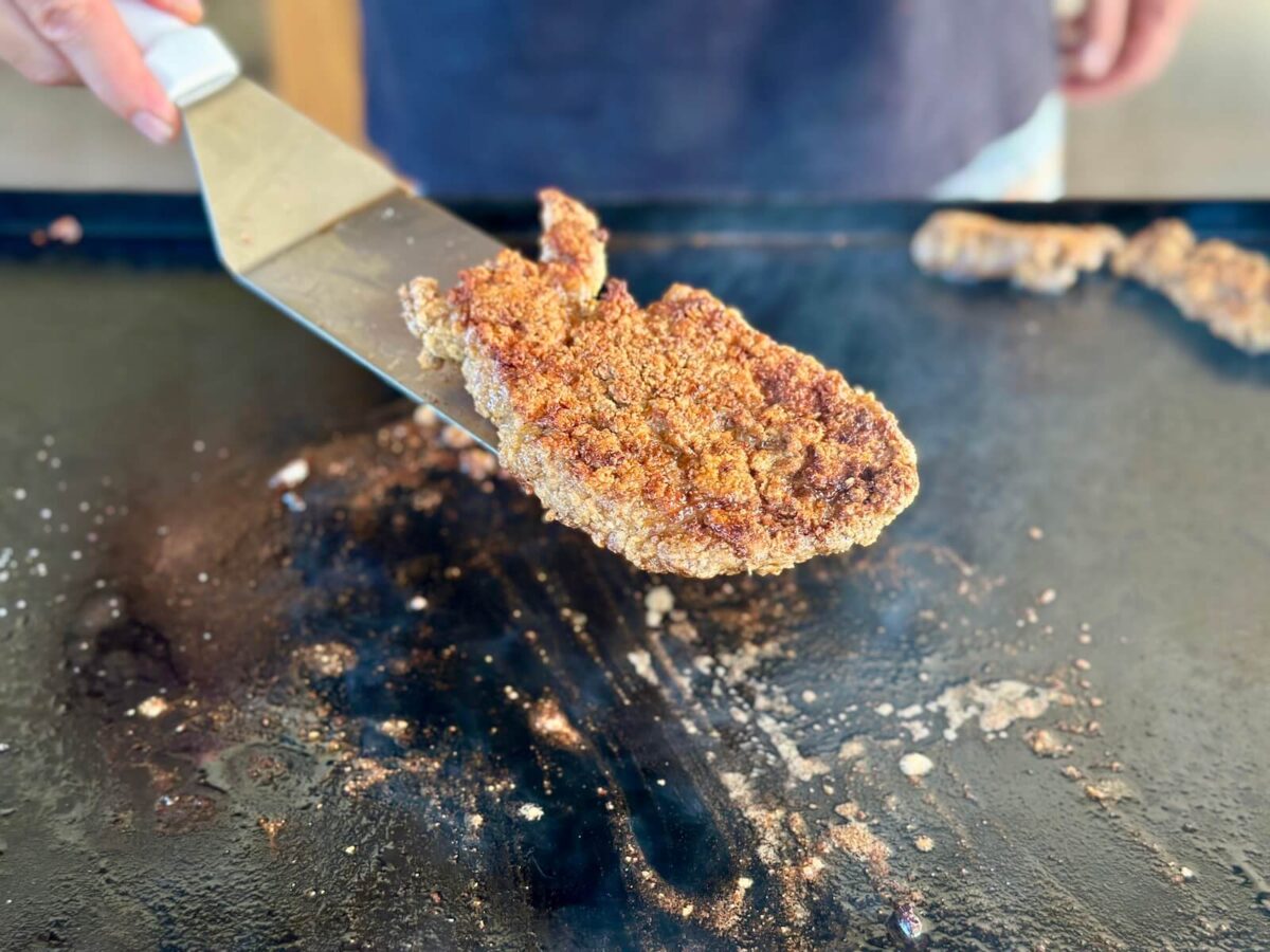 using a spatula to remove a piece of country fried steak from a griddle