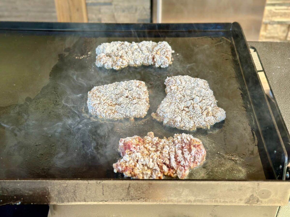 frying pieces of flour-coated chicken fried steak on a Blackstone griddle