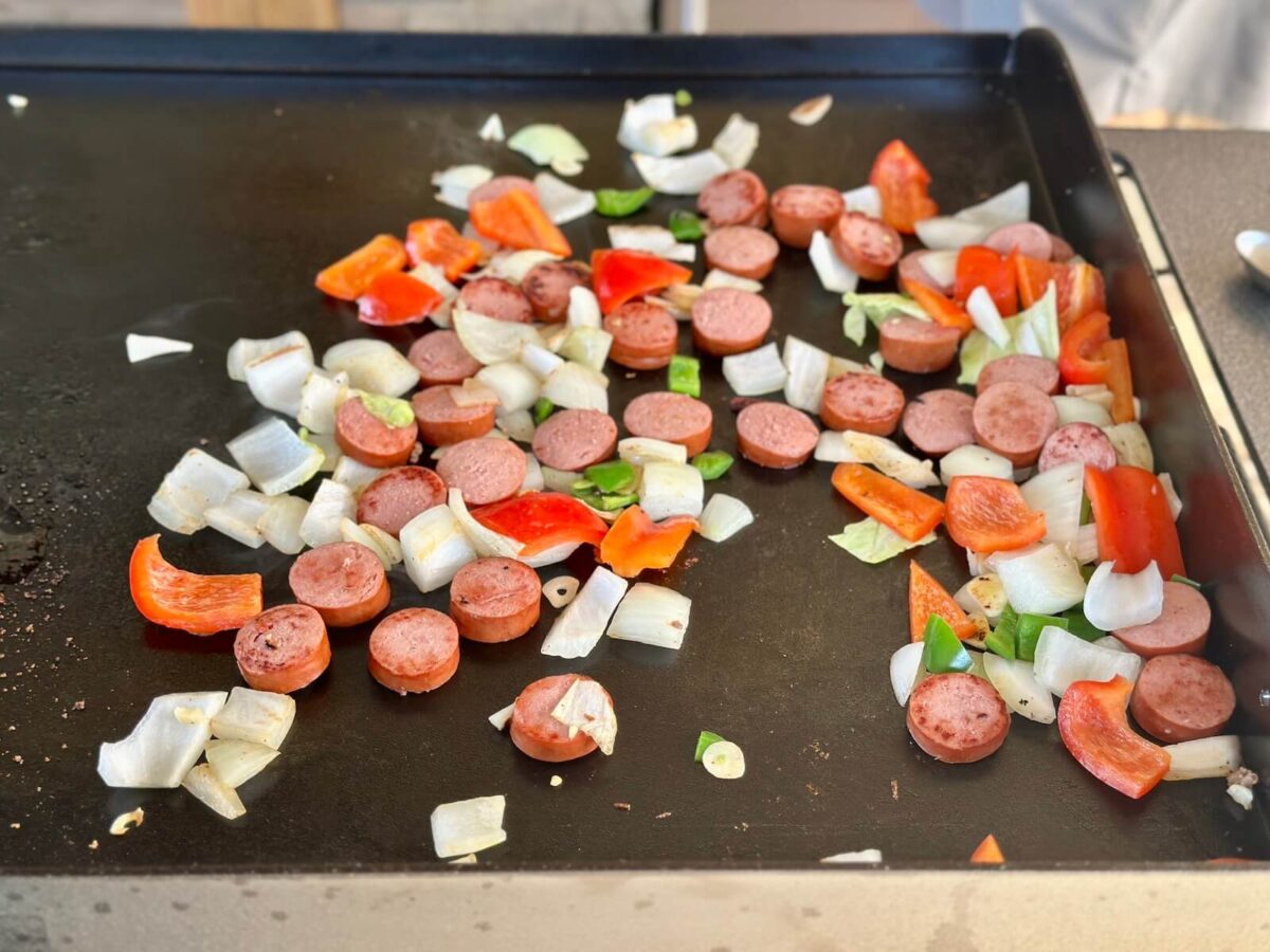 cooking slices of smoked sausage, onion, and bell peppers on a Blackstone griddle