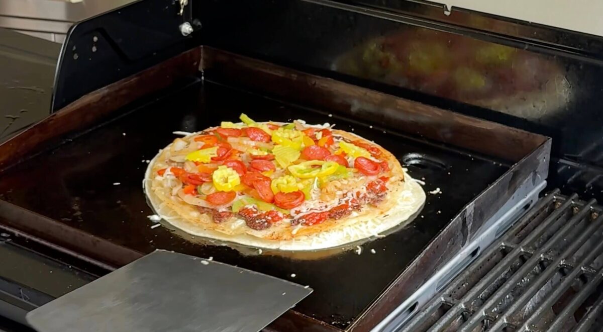 using a large spatula to remove a tortilla pizza from a griddle
