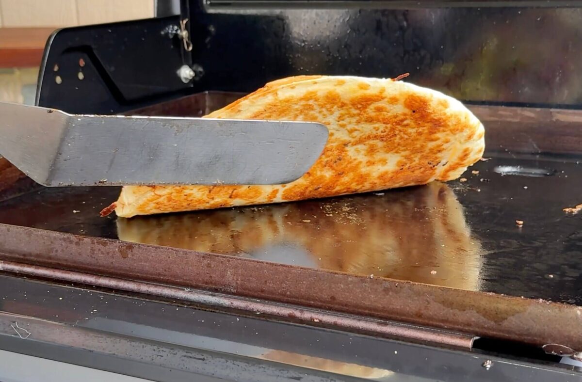 using a griddle spatula to check for a golden brown crust on a tortilla pizza