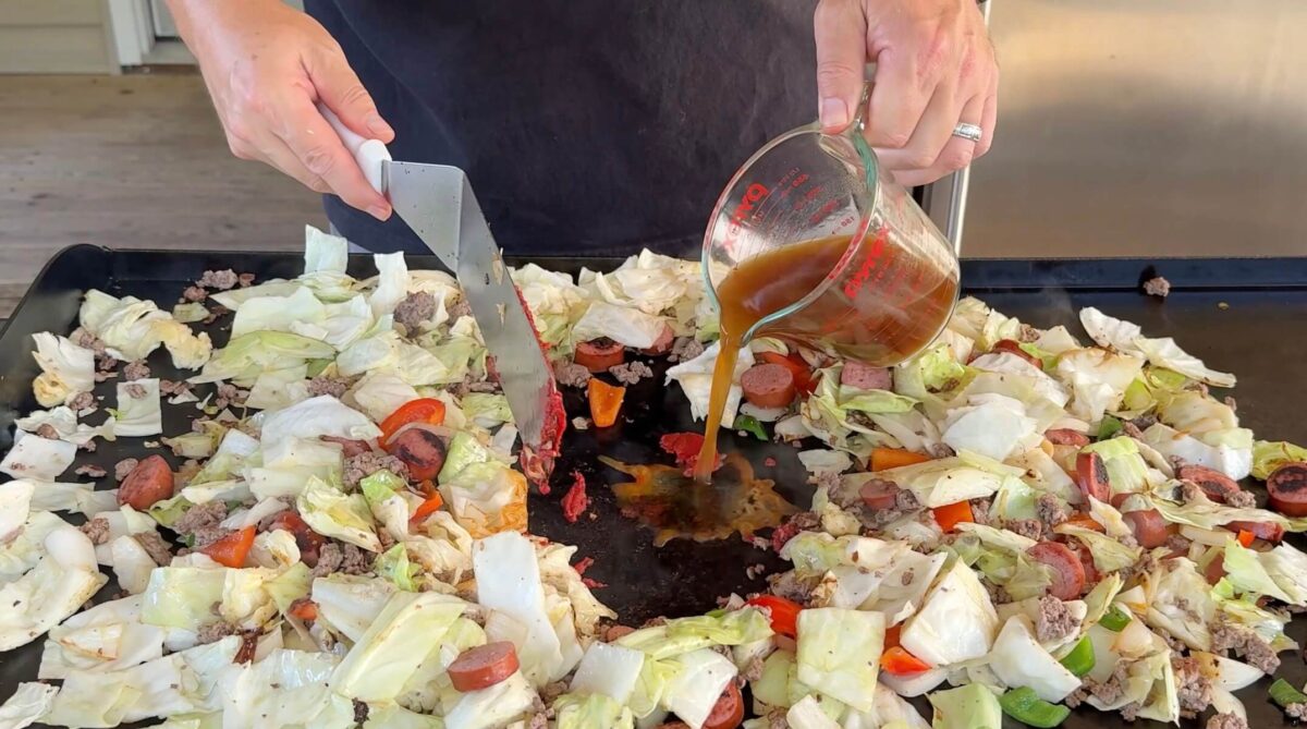adding tomato paste and beef broth to the griddle with dirty cabbage