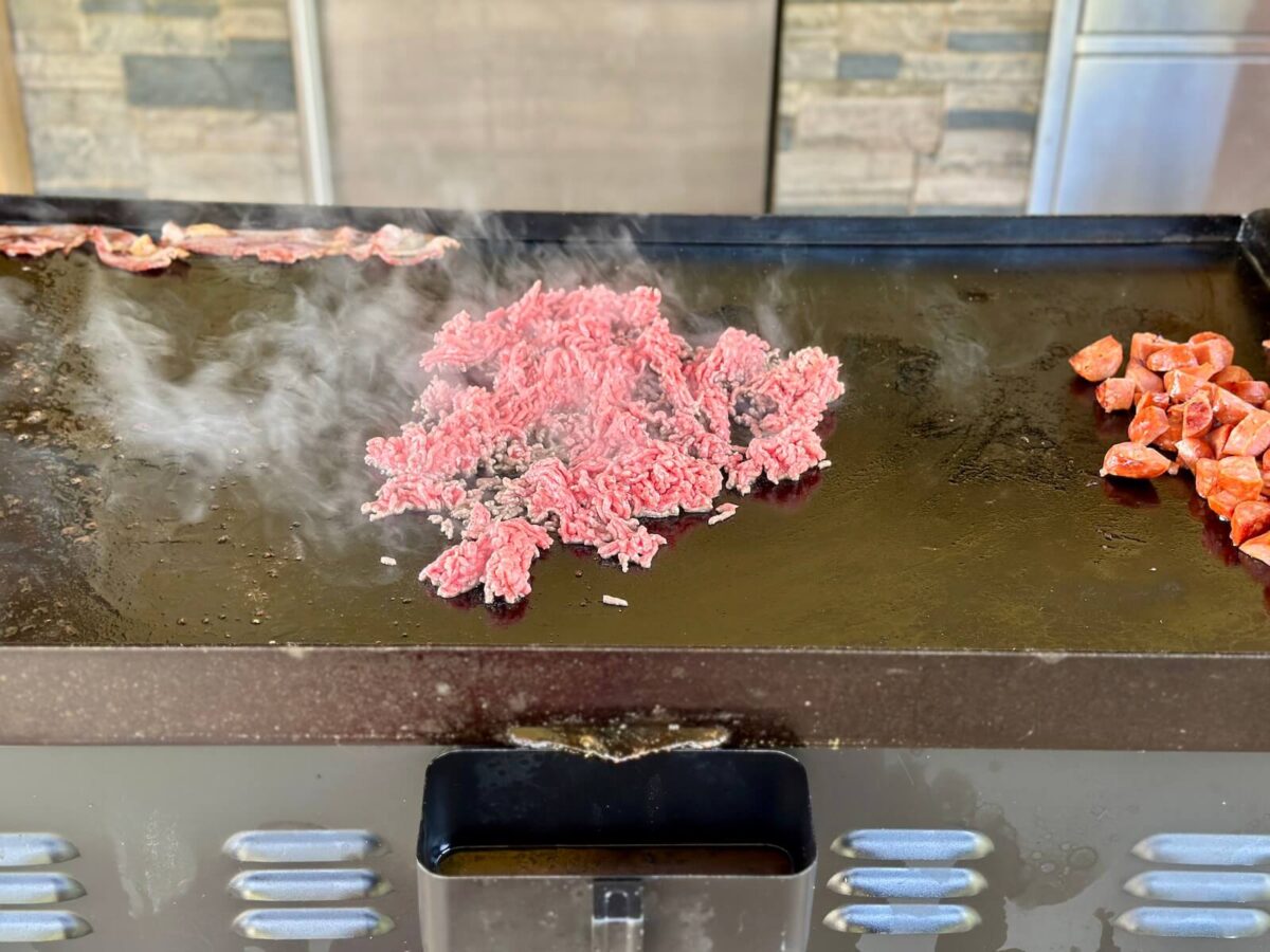 cooking ground beef, bacon, and andouille sausage on a Blackstone griddle