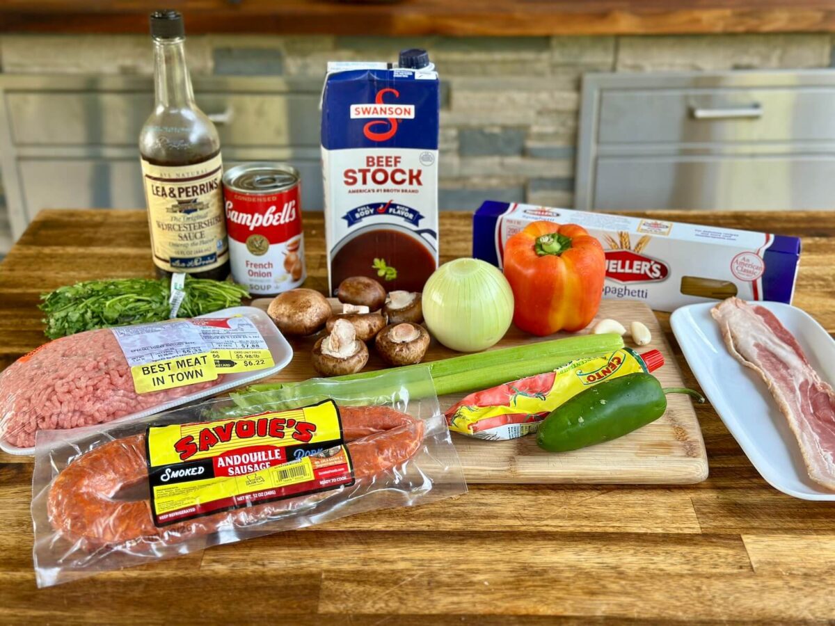 ingredients for dirty spaghetti including ground beef, andouille sausage, bacon, spaghetti noodles, vegetables, tomato paste, and Worcestershire sauce
