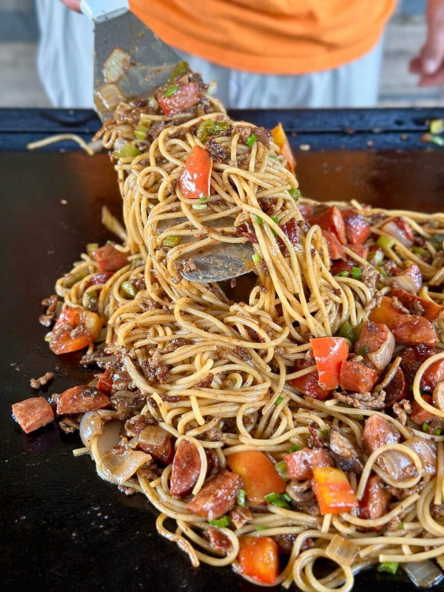 dirty spaghetti with ground beef, andouille sausage, and vegetables cooking on a griddle