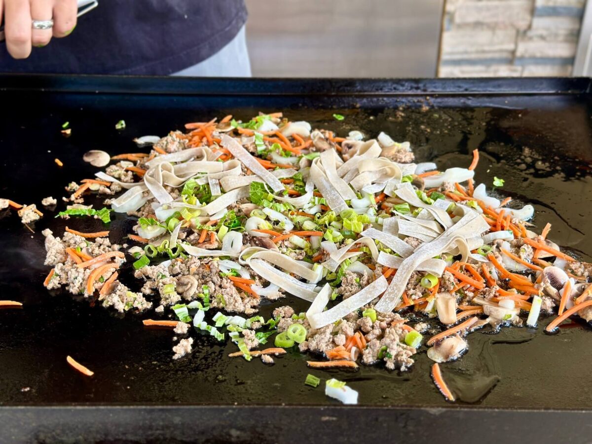 cooking ground pork, vegetables, and noodles on a griddle for dumpling in a bowl