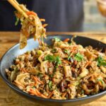 dumpling in a bowl with ground pork, wonton noodles, shredded carrots, and cilantro