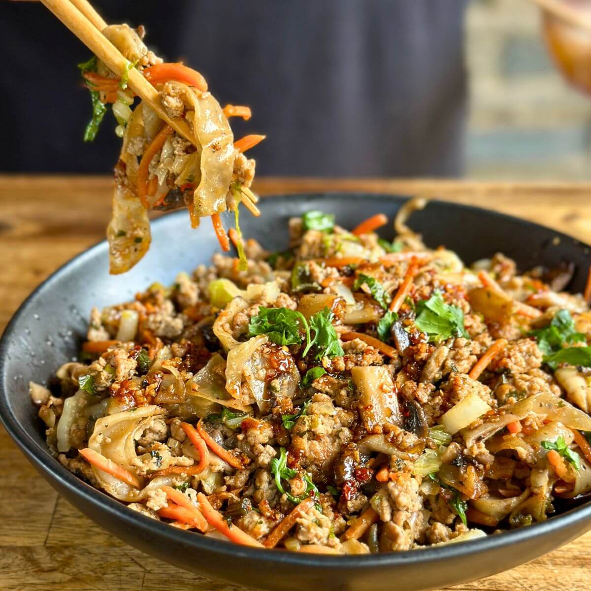 dumpling in a bowl with ground pork, wonton noodles, shredded carrots, and cilantro