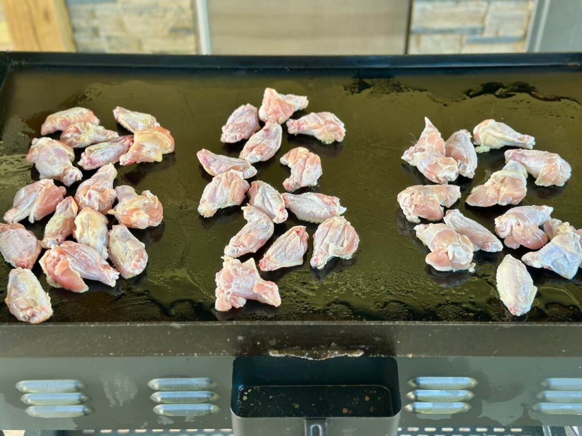 cooking chicken wings on a blackstone griddle in 3 separate areas