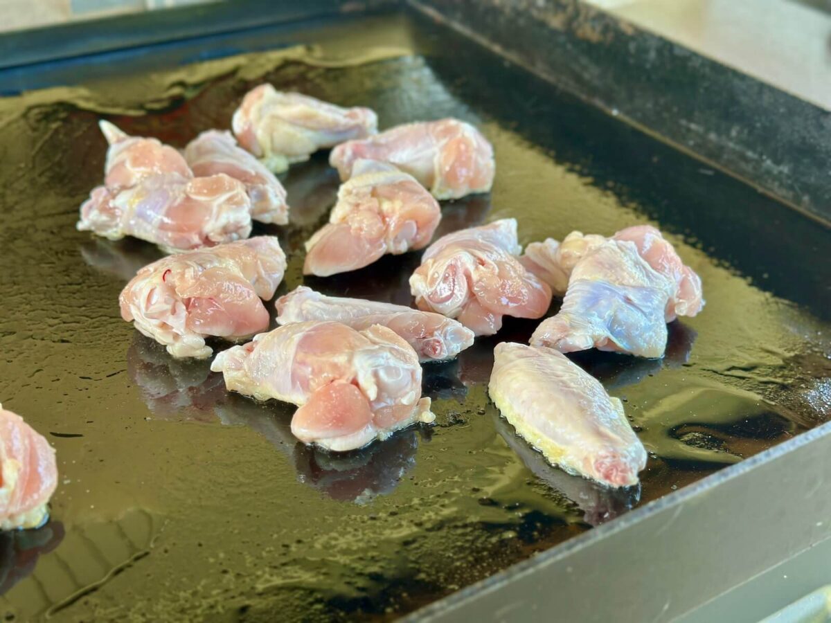 cooking chicken wings on an oiled griddle surface
