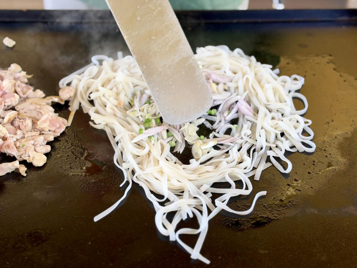 sauteeing garlic and shallots in the center of rice noodles on a Blackstone griddle