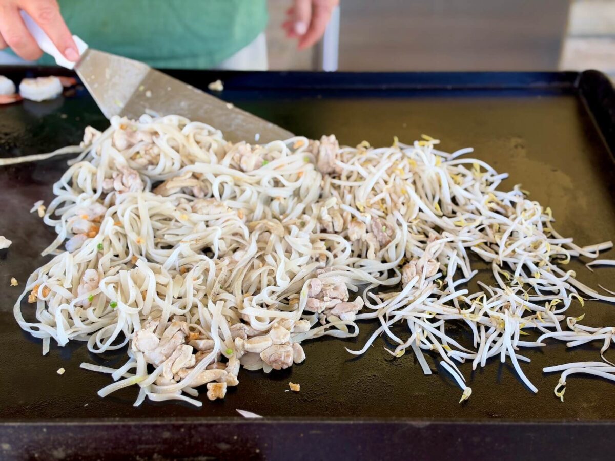 mixing chicken, rice noodles, and garlic on a Blackstone griddle