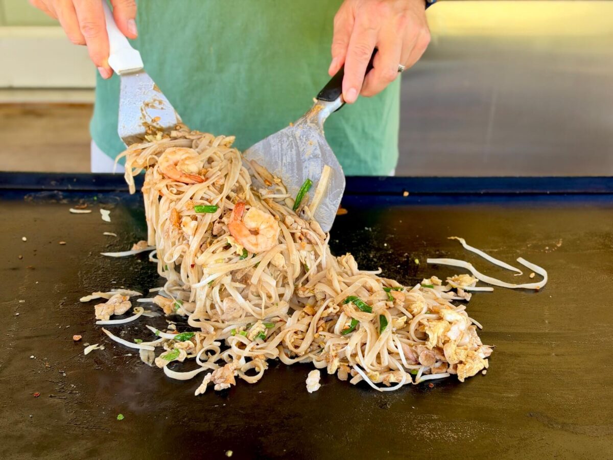 using two spatulas to mix pad thai on a Blackstone griddle