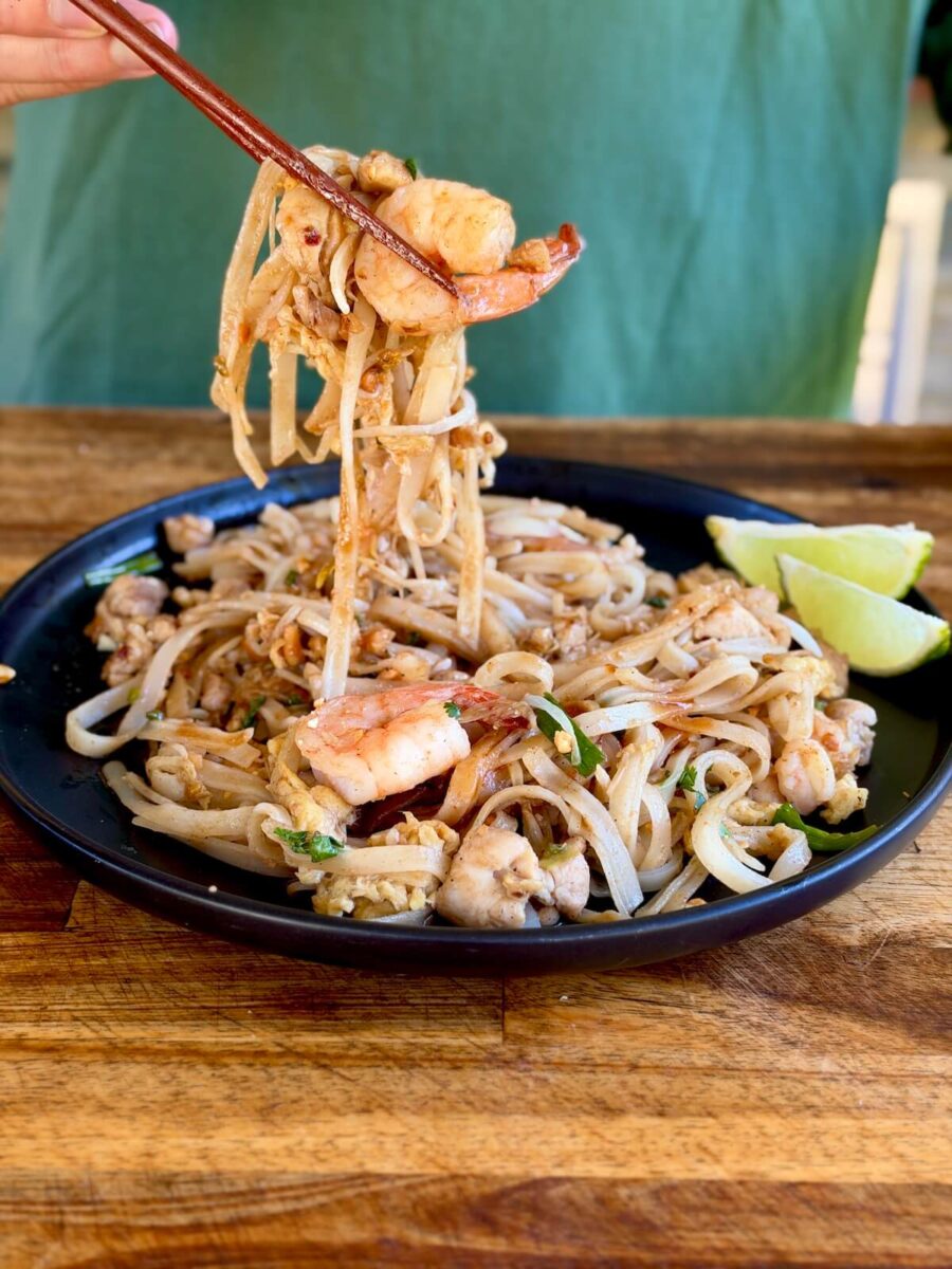 using chopsticks to eat shrimp and chicken Pad Thai