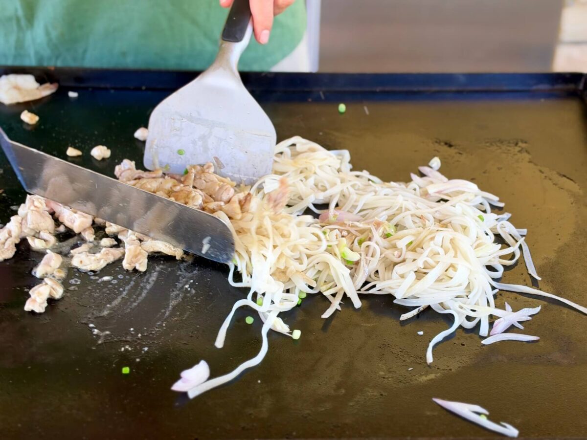 mixing chicken into cooked rice noodles on a Blackstone griddle