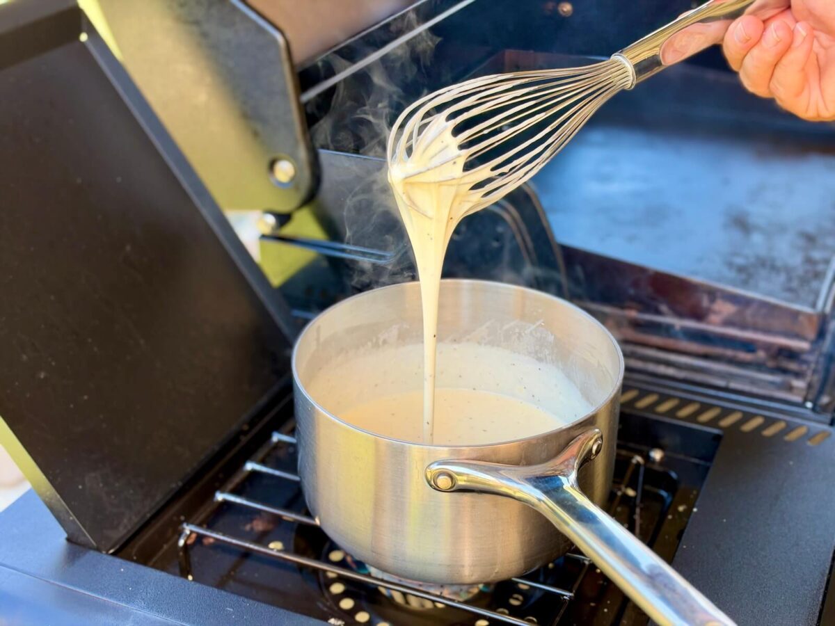 using a whisk to stir a saucepan of melted cheese sauce